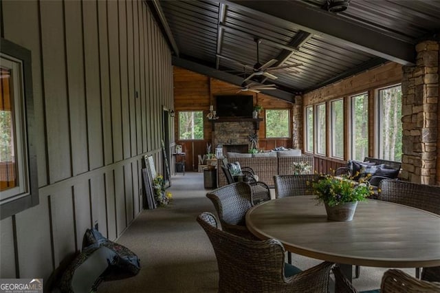 sunroom / solarium with ceiling fan, lofted ceiling with beams, wood ceiling, and a stone fireplace