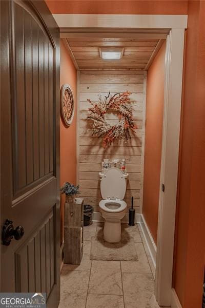 bathroom with toilet, wood walls, and wooden ceiling