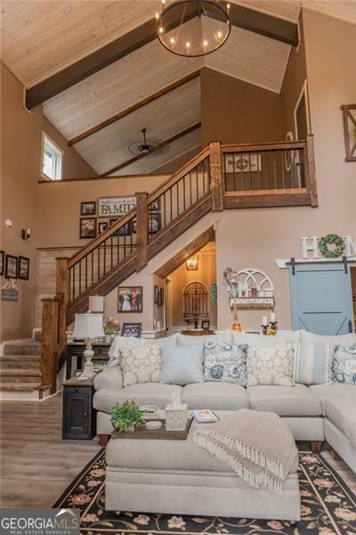 living room with wood ceiling, hardwood / wood-style floors, a barn door, high vaulted ceiling, and beamed ceiling