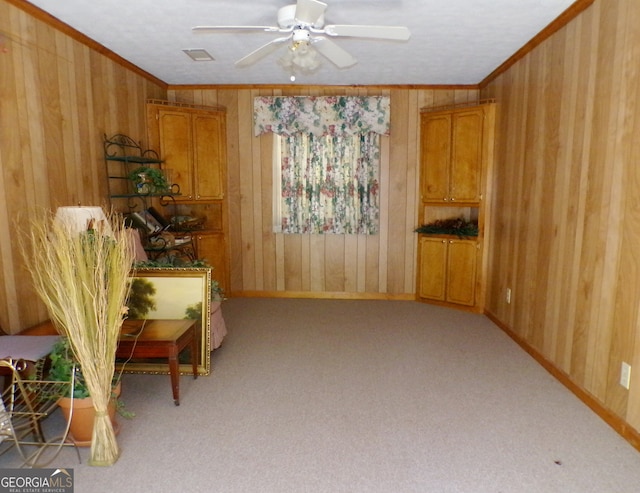 sitting room with ceiling fan, light colored carpet, wooden walls, and ornamental molding