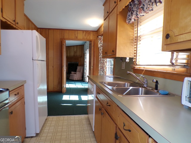 kitchen with wooden walls, white appliances, sink, and light colored carpet