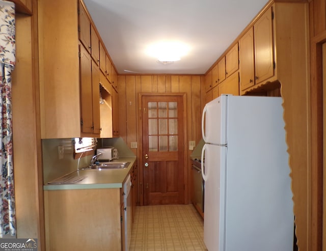 kitchen with light brown cabinetry, white refrigerator, wood walls, and sink