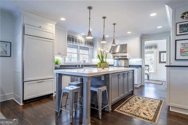 kitchen featuring pendant lighting, wall chimney range hood, dark wood-type flooring, and a center island