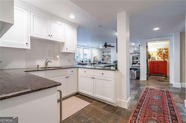 kitchen featuring ceiling fan, dark stone countertops, sink, kitchen peninsula, and white cabinets