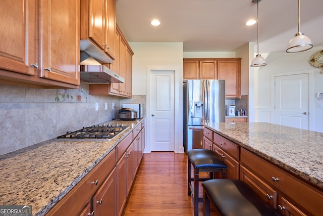 kitchen with a kitchen breakfast bar, dark hardwood / wood-style floors, stainless steel appliances, light stone countertops, and hanging light fixtures