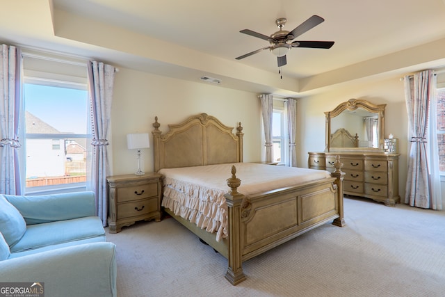 bedroom featuring ceiling fan, a tray ceiling, and light carpet