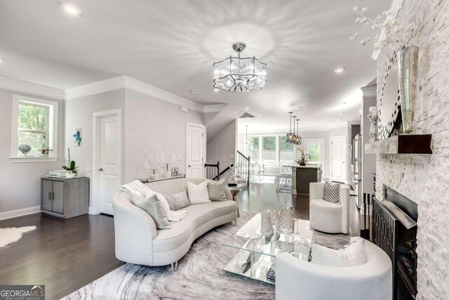 living room with crown molding, a stone fireplace, an inviting chandelier, and dark hardwood / wood-style flooring