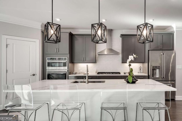 kitchen featuring pendant lighting, appliances with stainless steel finishes, wall chimney exhaust hood, and sink