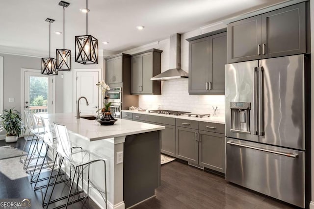 kitchen featuring an island with sink, decorative light fixtures, wall chimney exhaust hood, dark wood-type flooring, and appliances with stainless steel finishes