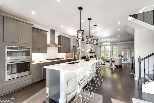 kitchen featuring wall chimney exhaust hood, gray cabinets, a breakfast bar, stainless steel appliances, and hanging light fixtures