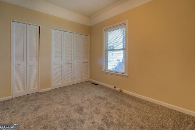 unfurnished bedroom featuring crown molding, multiple closets, and light colored carpet