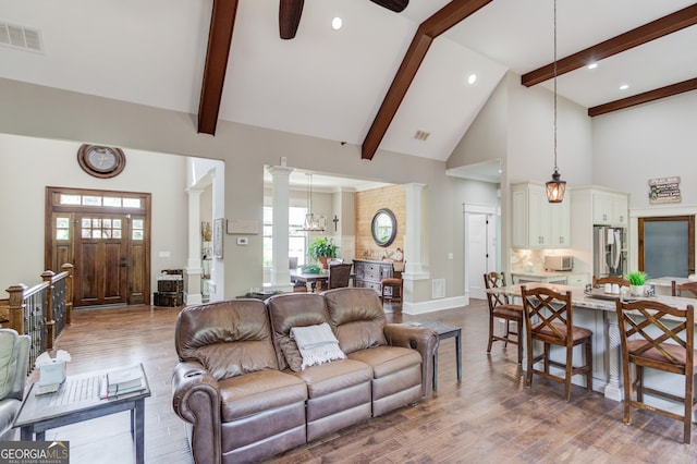 living room featuring ornate columns, wood-type flooring, and high vaulted ceiling