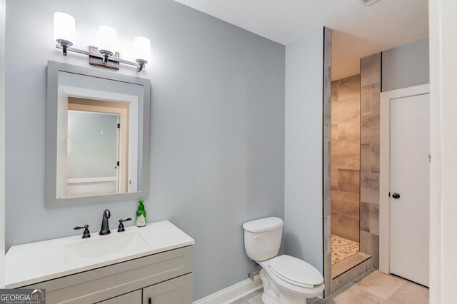 bathroom featuring vanity, toilet, tiled shower, and tile patterned flooring