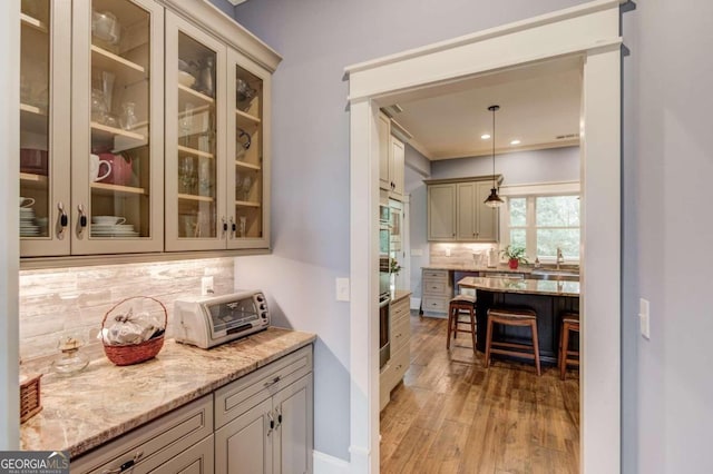 bar with decorative backsplash, oven, light hardwood / wood-style flooring, light stone countertops, and pendant lighting