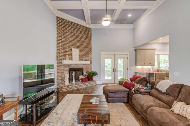 living room featuring wood-type flooring, a fireplace, french doors, coffered ceiling, and beam ceiling