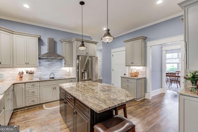 kitchen with wall chimney range hood, light wood-type flooring, high end fridge, crown molding, and a center island