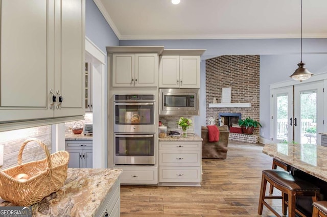 kitchen featuring french doors, stainless steel appliances, light stone countertops, a brick fireplace, and light wood-type flooring