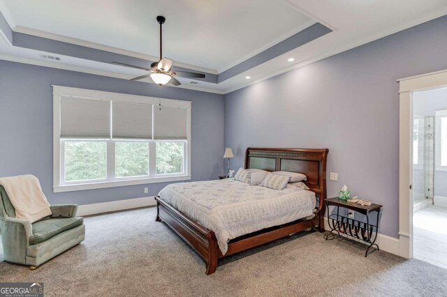 carpeted bedroom with ceiling fan, crown molding, a tray ceiling, and ensuite bathroom