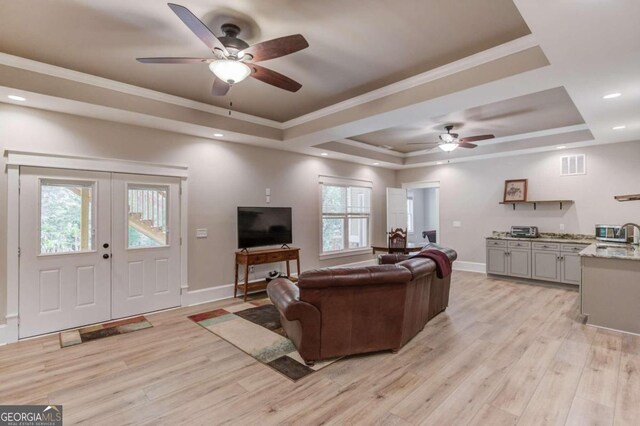 living room with plenty of natural light, ceiling fan, a tray ceiling, and light wood-type flooring