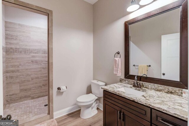 bathroom with vanity, toilet, hardwood / wood-style flooring, and tiled shower