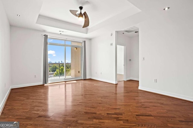 unfurnished room featuring ceiling fan, a tray ceiling, and dark hardwood / wood-style flooring