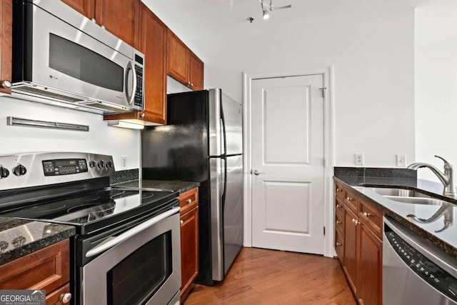 kitchen featuring sink, stainless steel appliances, light hardwood / wood-style floors, and dark stone counters