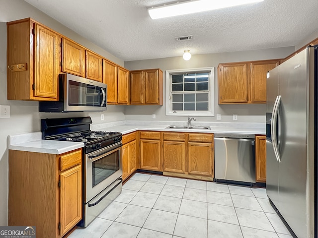 kitchen featuring light tile patterned floors, a textured ceiling, appliances with stainless steel finishes, and sink