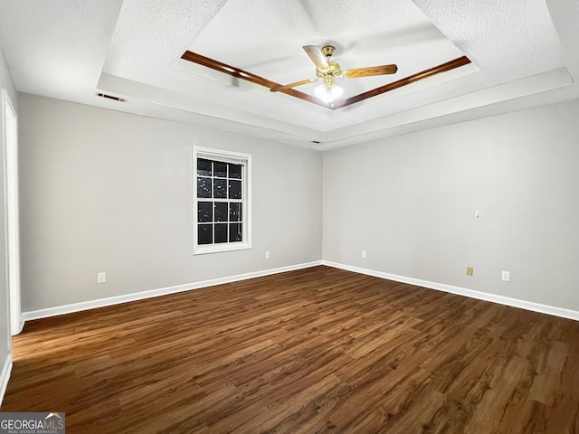 empty room with a raised ceiling, ceiling fan, a textured ceiling, and dark hardwood / wood-style flooring