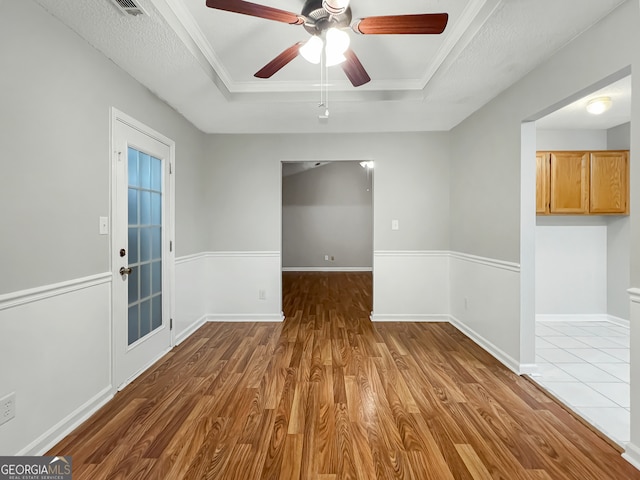 empty room with a textured ceiling, hardwood / wood-style flooring, a tray ceiling, and ceiling fan