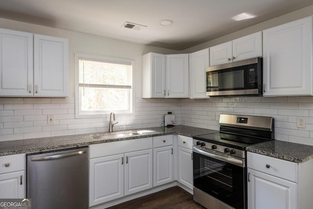 kitchen featuring sink, white cabinetry, stainless steel appliances, dark stone counters, and decorative backsplash