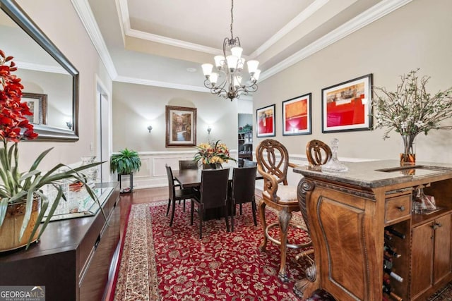 dining area featuring dark wood-type flooring, a notable chandelier, ornamental molding, and a raised ceiling