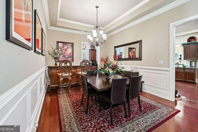 dining space featuring a notable chandelier, ornamental molding, a tray ceiling, and dark hardwood / wood-style flooring