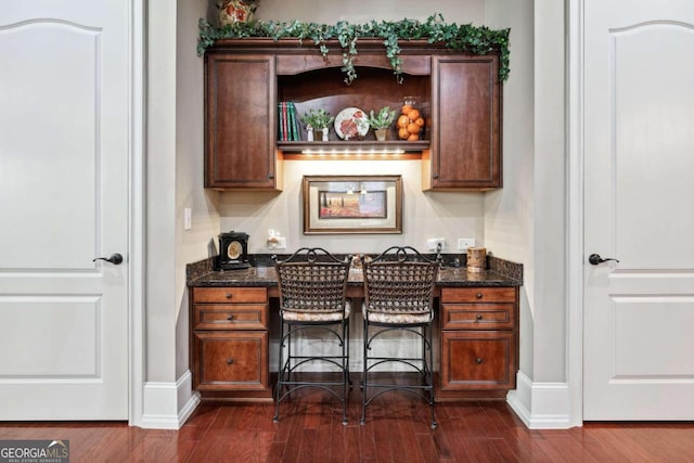 bar with dark hardwood / wood-style flooring and dark stone counters