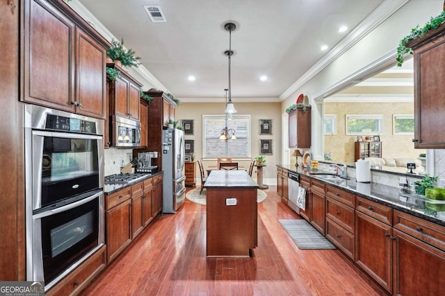 kitchen with wood-type flooring, stainless steel appliances, crown molding, decorative light fixtures, and a center island