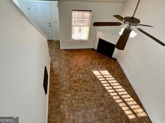 unfurnished living room with ceiling fan, a fireplace, and baseboards