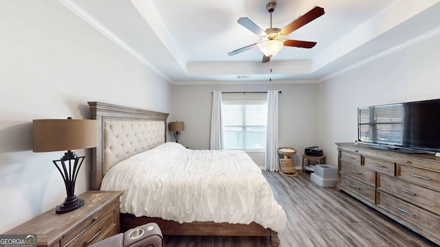 bedroom with hardwood / wood-style floors, crown molding, a tray ceiling, and ceiling fan