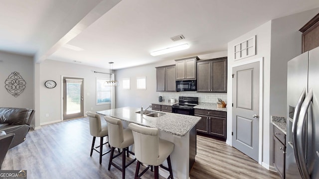 kitchen featuring a center island with sink, black appliances, hanging light fixtures, and light hardwood / wood-style floors