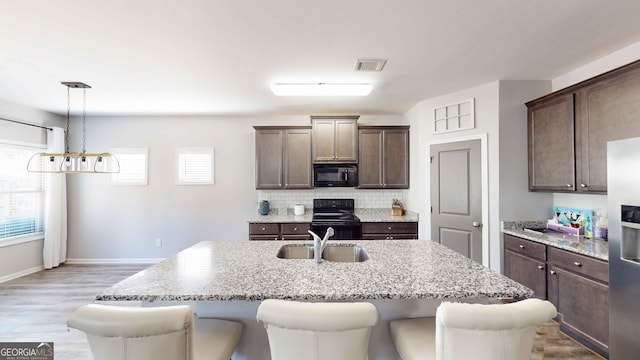 kitchen featuring a kitchen island with sink, light hardwood / wood-style flooring, hanging light fixtures, black appliances, and tasteful backsplash