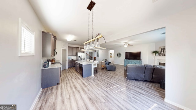 kitchen featuring stainless steel fridge, dark brown cabinets, a center island with sink, a kitchen bar, and pendant lighting