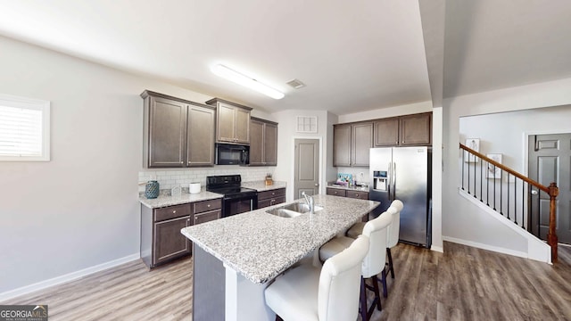 kitchen featuring black appliances, dark brown cabinets, hardwood / wood-style floors, a breakfast bar, and a kitchen island with sink