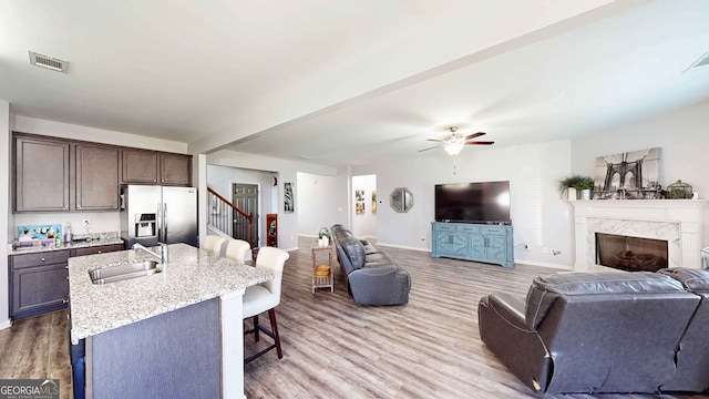 kitchen with sink, an island with sink, a high end fireplace, light hardwood / wood-style floors, and stainless steel fridge with ice dispenser