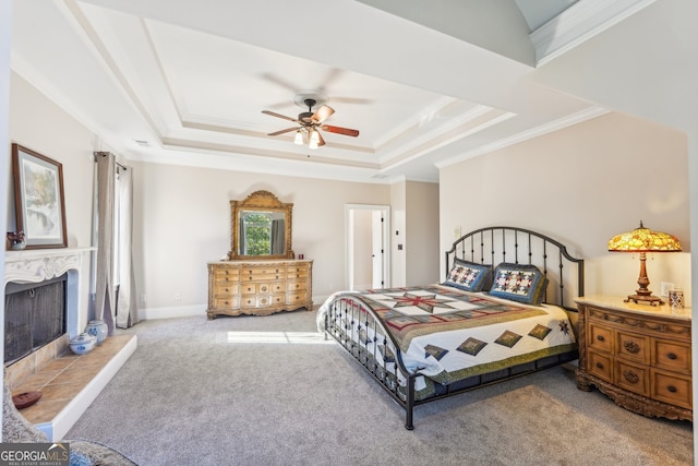 carpeted bedroom with crown molding, a tiled fireplace, a tray ceiling, and ceiling fan