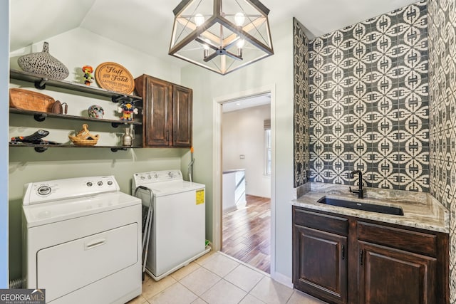 laundry room with washing machine and dryer, sink, light hardwood / wood-style floors, cabinets, and an inviting chandelier