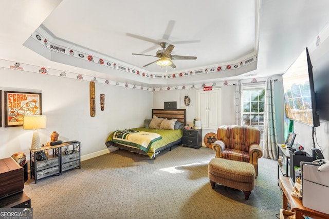 carpeted bedroom with a raised ceiling and ceiling fan