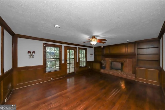 unfurnished living room with ceiling fan, a fireplace, a textured ceiling, and dark hardwood / wood-style flooring