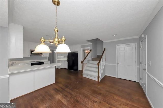 kitchen with dark hardwood / wood-style floors, black fridge, kitchen peninsula, decorative light fixtures, and white cabinetry