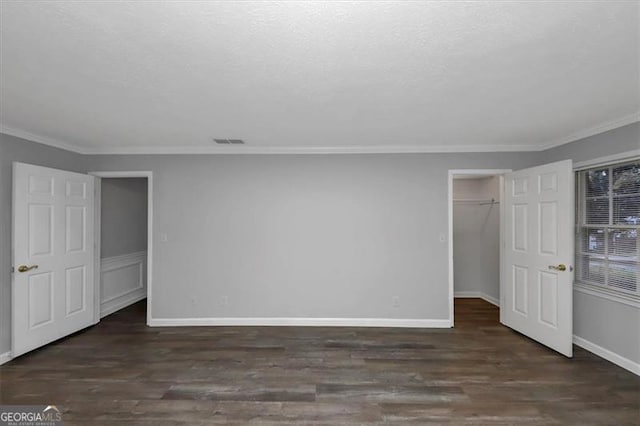 unfurnished bedroom with a textured ceiling, a spacious closet, ornamental molding, dark hardwood / wood-style floors, and a closet