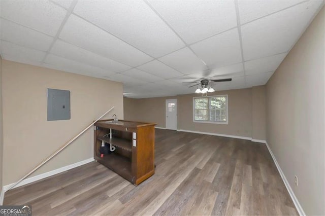 interior space featuring electric panel, a drop ceiling, wood-type flooring, and ceiling fan