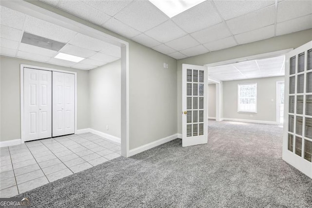 basement featuring french doors, light tile patterned flooring, and a drop ceiling