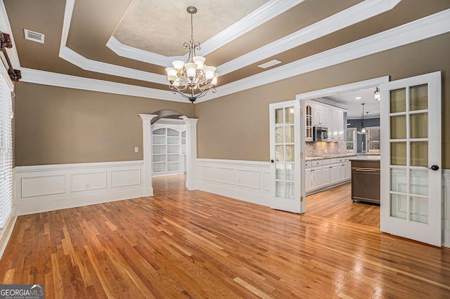 unfurnished dining area featuring light hardwood / wood-style flooring, a tray ceiling, ornamental molding, decorative columns, and an inviting chandelier